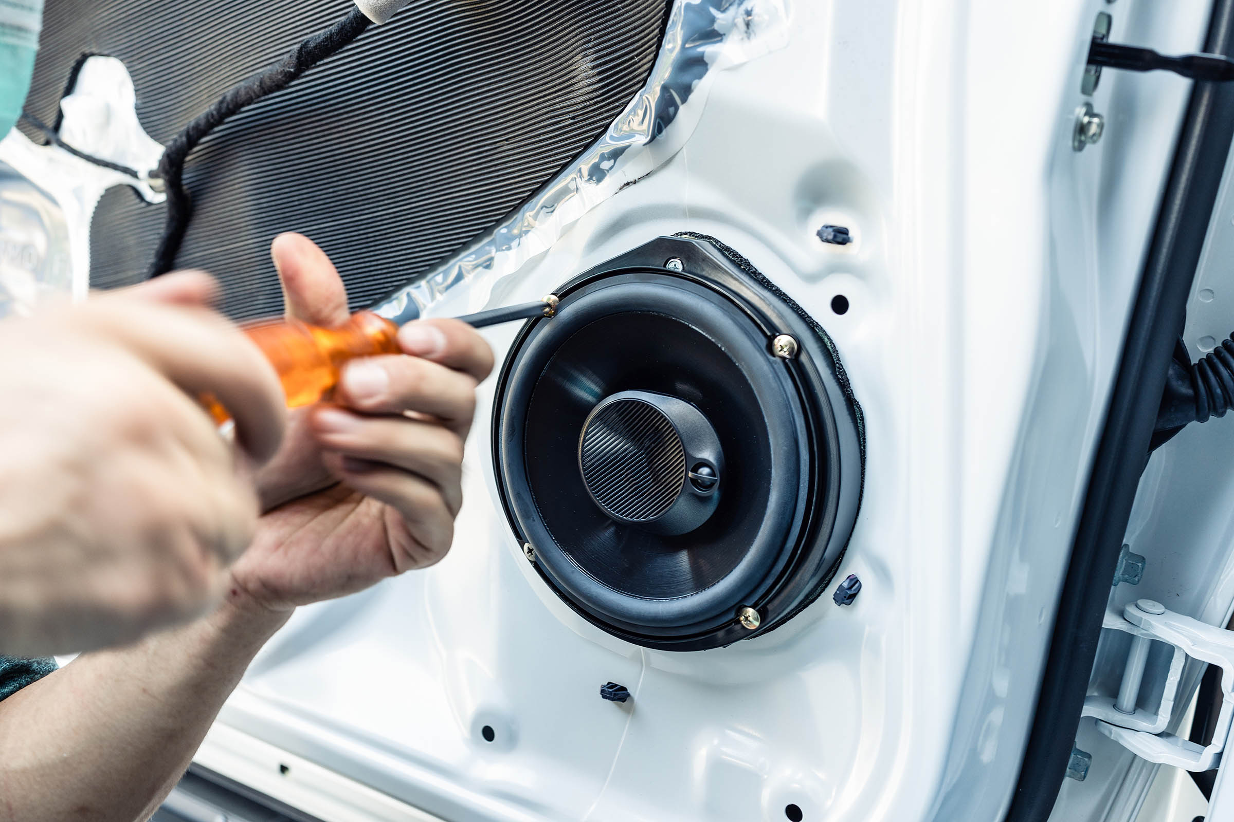 Hands using a screwdriver to install a round speaker in a car door panel.