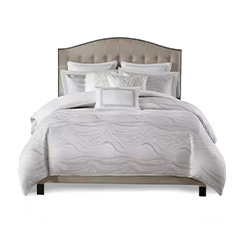 Elegant bed with a tufted headboard, adorned with white and patterned pillows, and a textured white comforter.