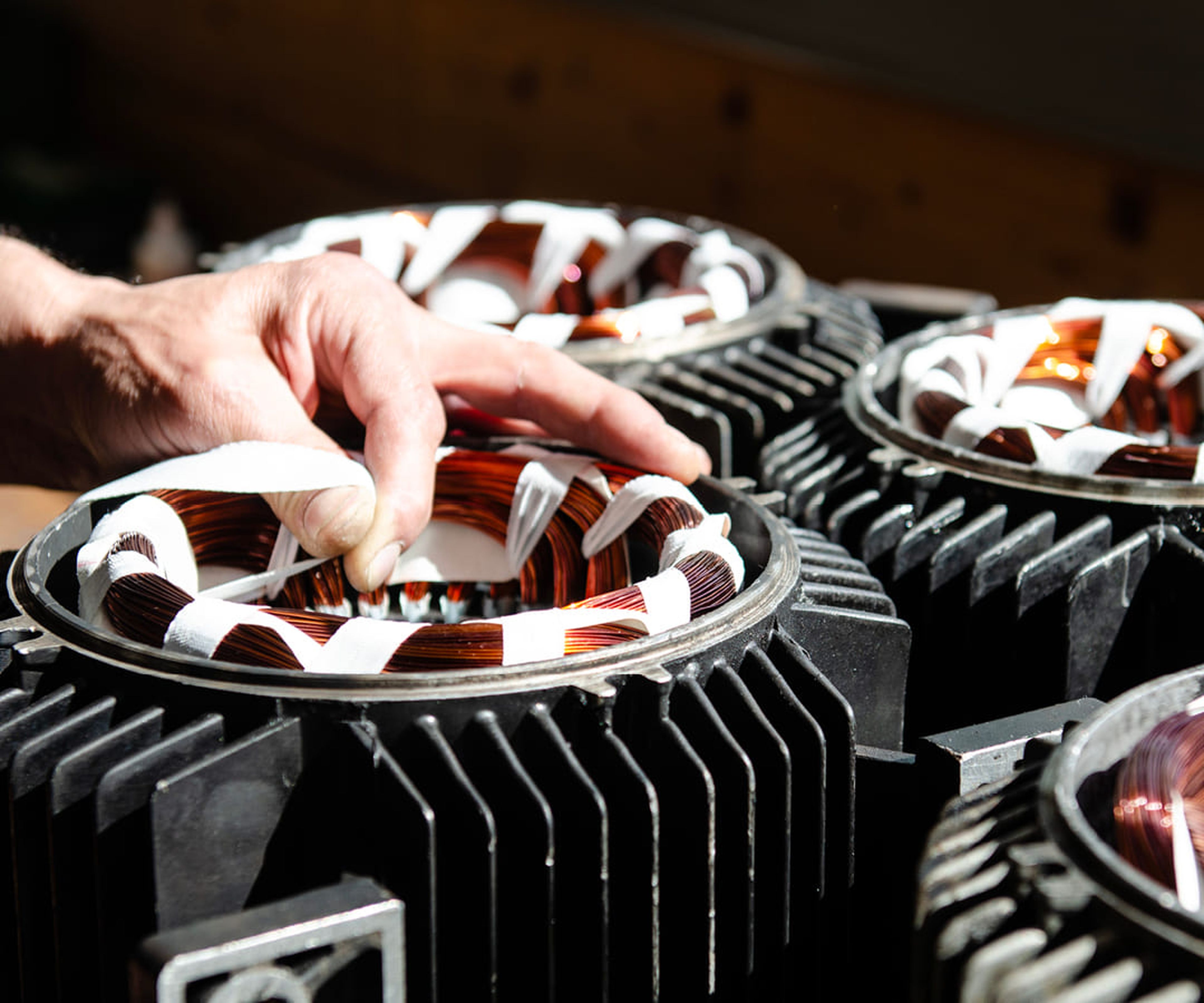 Handjustierung von Kupferspulen an Industriemaschinen mit schwarzen Metallrippen, in hellem Sonnenlicht.