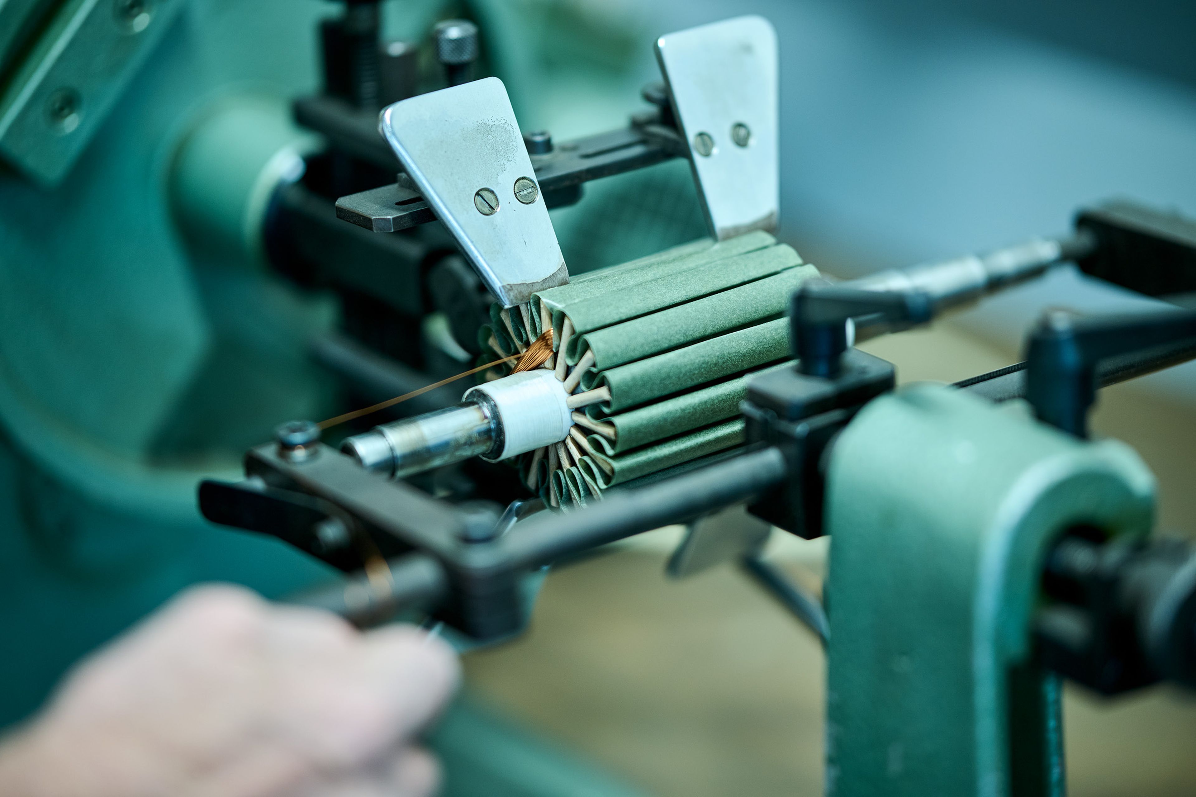 Nahaufnahme einer grünen Industriemaschine, die Kupferdraht um einen zylindrischen Kern wickelt, wobei eine Hand den Mechanismus einstellt.