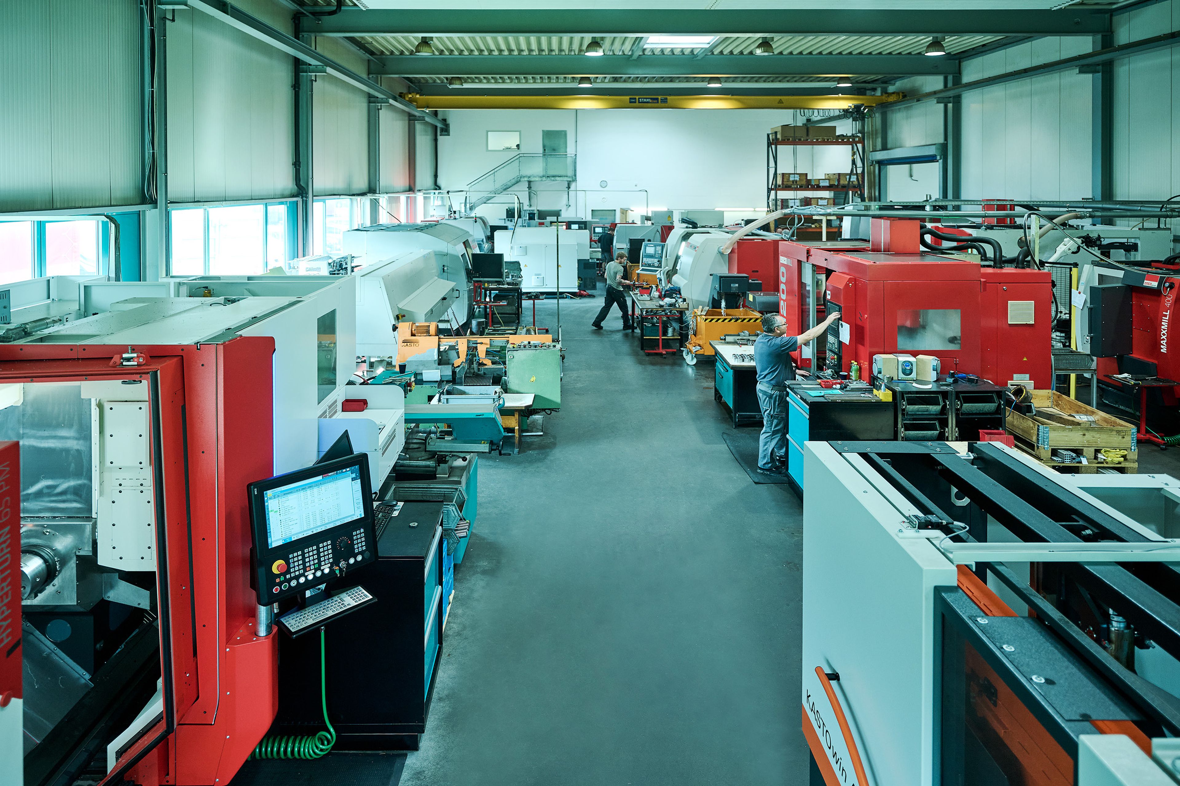 Geräumige Industriewerkstatt mit mehreren roten und weißen Maschinen, einer Computerstation und Arbeitern, die Geräte bedienen.