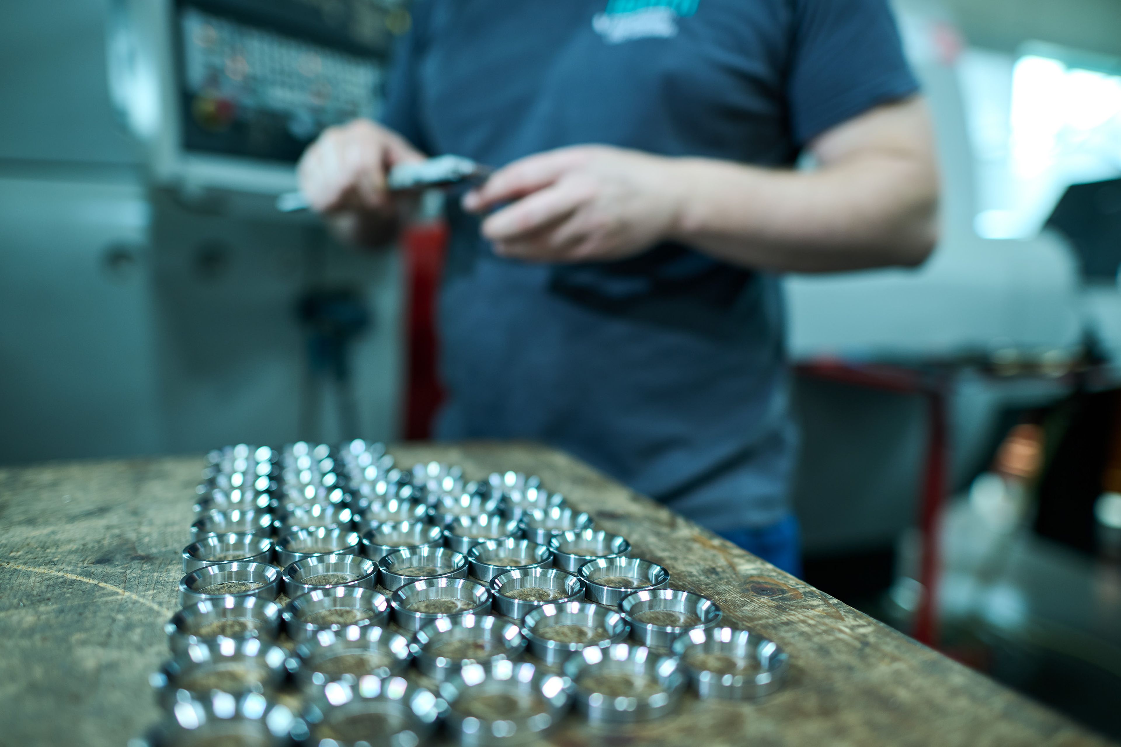 Person, die Metallringe mit einem Messschieber auf einer Werkbank misst, mit Reihen von glänzenden Ringen im Vordergrund.