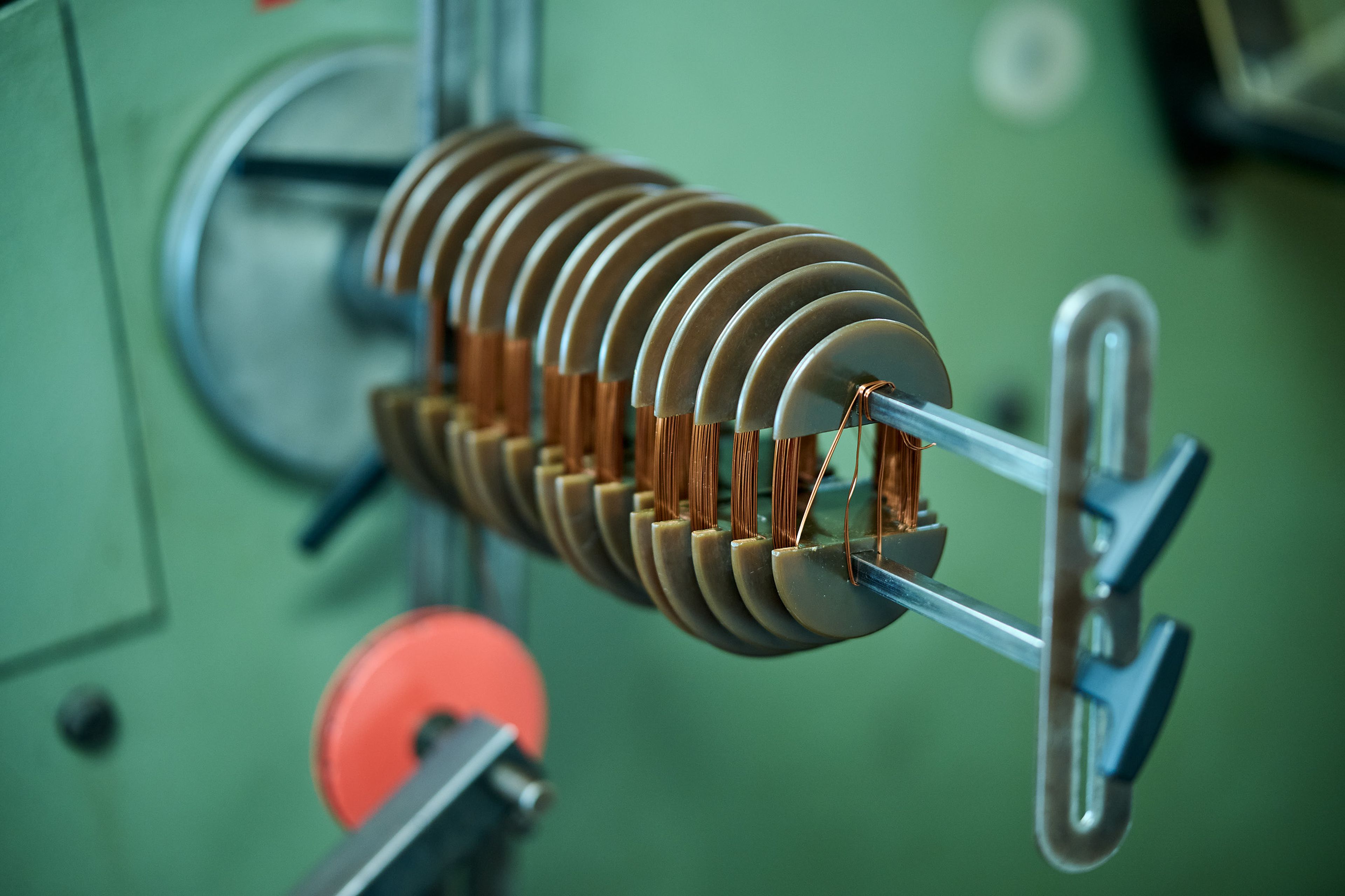 Nahaufnahme eines komplexen Maschinenteils mit mehreren Metallscheiben und Kupferdrähten vor einem unscharfen grünen Hintergrund.
