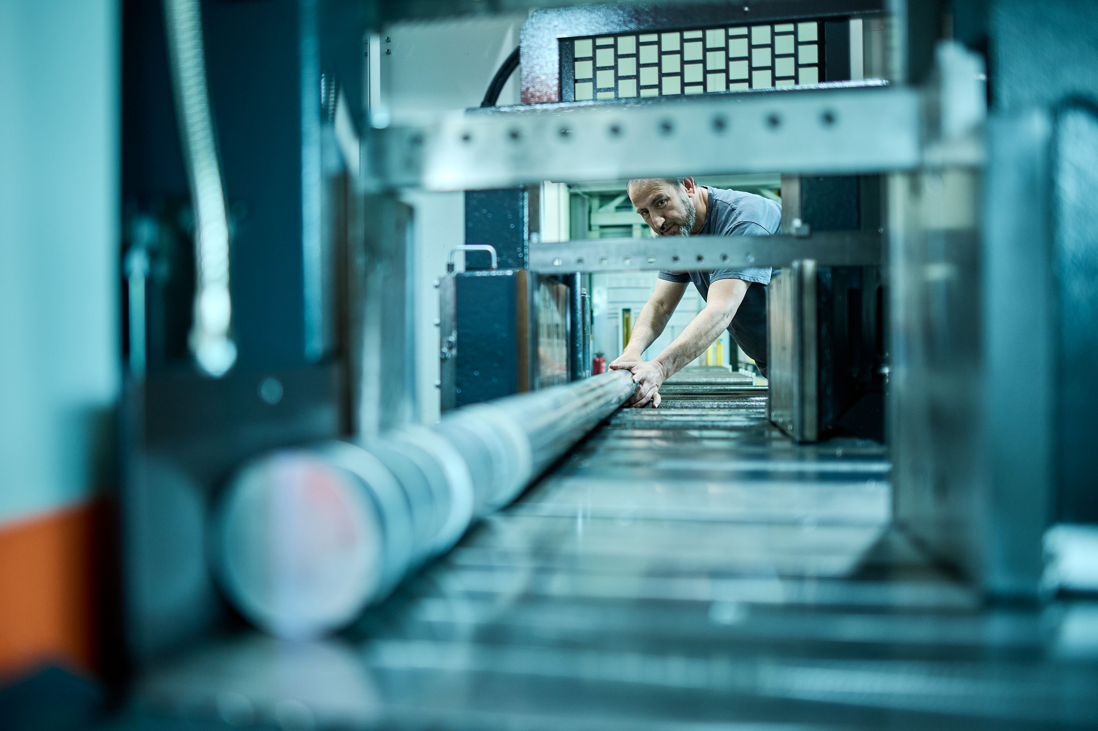 Ein Mann bedient eine große Industriemaschine, in der er mit konzentrierter Miene eine lange Metallstange einstellt.