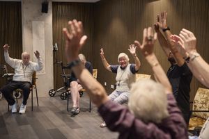Activiteitenruimte met ouderen op stoelen. Ze hebben allemaal beide armen omhoog.