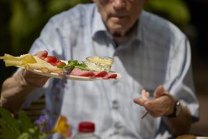 Een meneer zit aan tafel met in zijn handen een bord met allerlei soorten broodbeleg.
