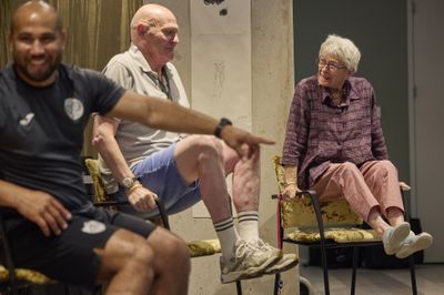 Twee oudere personen tillen duwen zichzelf op de leuningen van hun stoelen omhoog met hun benen in de lucht.
