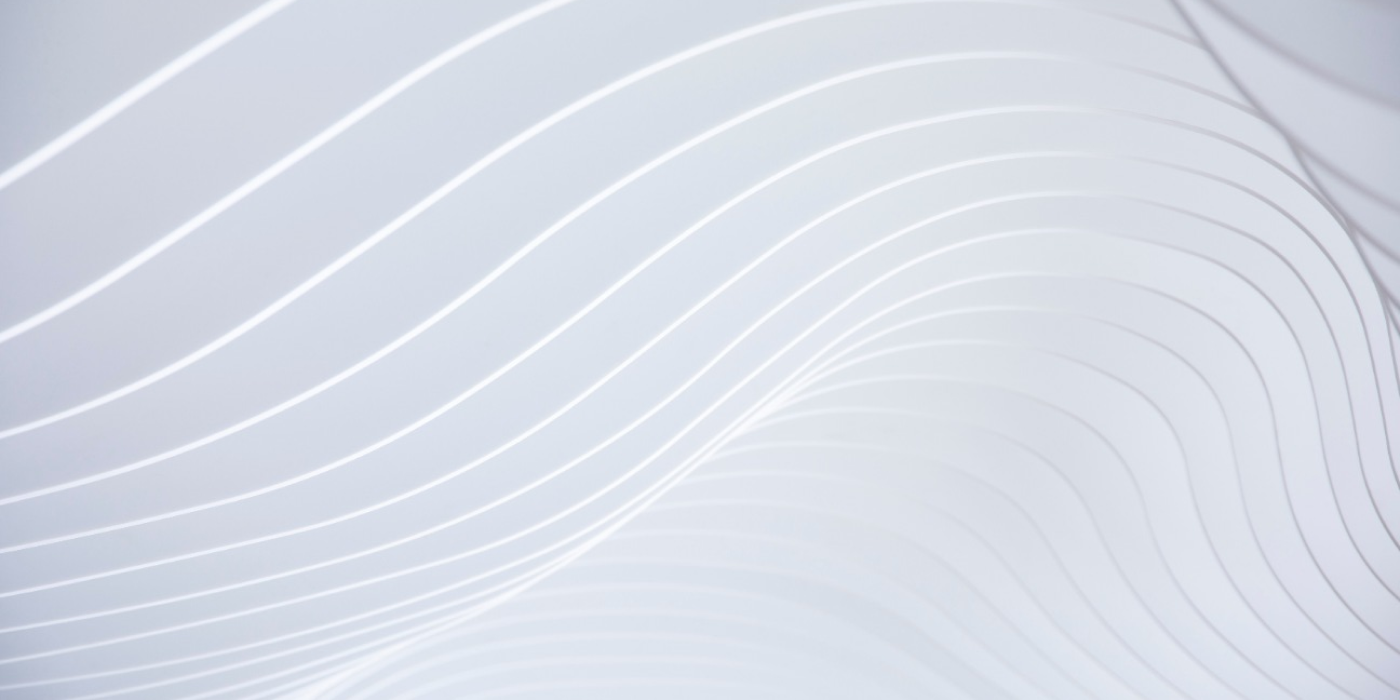 A close-up view of a white, curved architectural detail with repetitive wavy lines creating a sense of movement and texture.