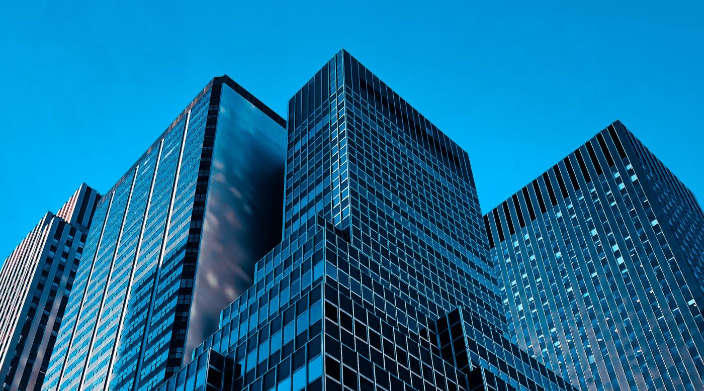 A panoramic view of modern skyscrapers with reflective glass facades against a clear blue sky, highlighting the geometric patterns and sleek urban design.