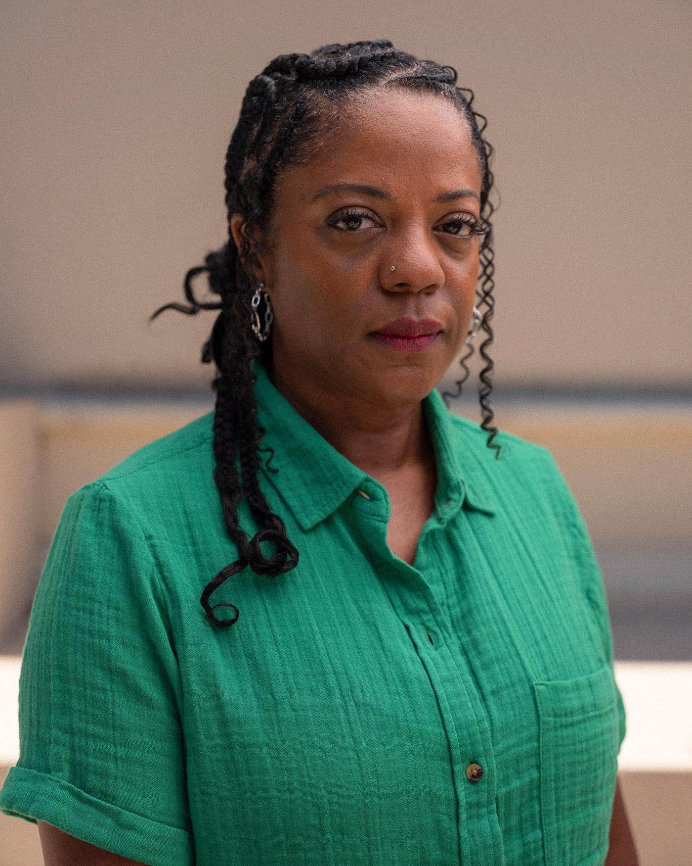 A person with braided hair wearing a green shirt looks directly at the camera.