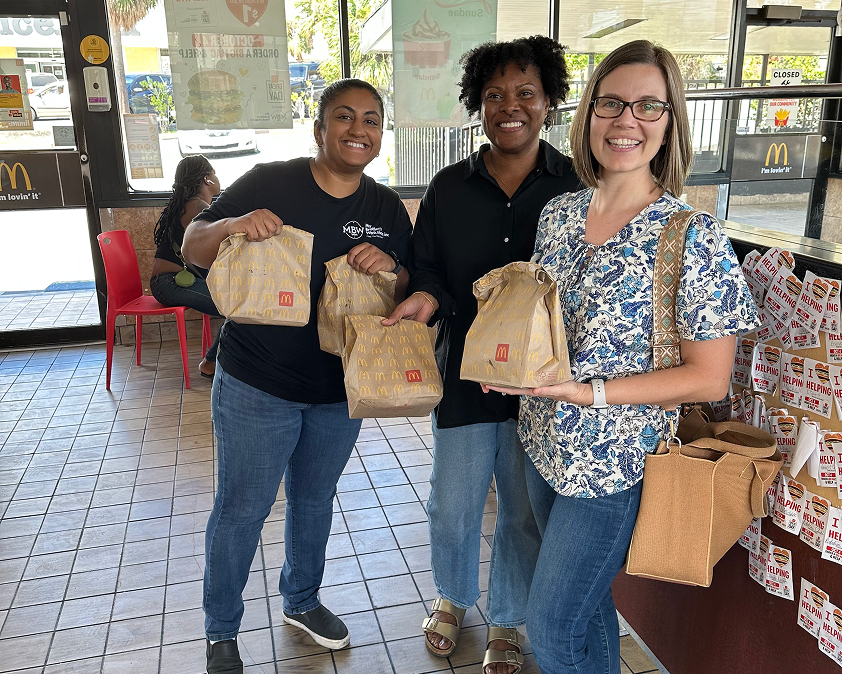 Three people smiling and holding McDonald's bags inside a restaurant.