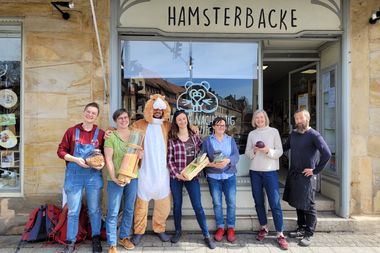 Das Team der Hamsterbacke posiert vor dem Laden. Ein Mensch trägt ein Hamsterkostüm.