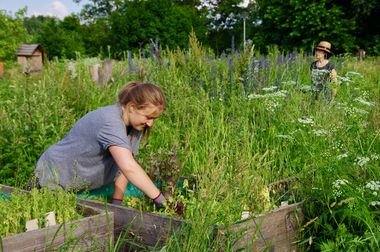 Eine Frau kniet vor einem Hochbeet in einer Anlage, die vor Grün nur so strotzt.