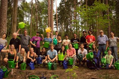 Eine große Gruppe Menschen im Wald mit Gießkannen.