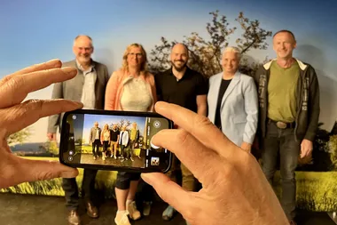 Ein Mensch macht ein Gruppenfoto mit dem Smartphone von Menschen vor einer Fotowand
