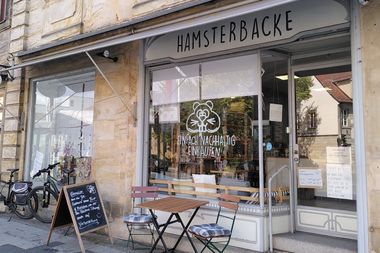 Der Laden Hamsterbacke von außen mit Stühlen und aufgestelltem Kreideschild. Im Schaufenster ist ein großer Hamsterkopf mit dem Schriftzug "Einfach nachhaltig einkaufen" aufgedruckt.