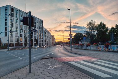 Eine leere Straße im Abendlicht, der Hohenzollernring in Bayreuth. Eine Ampel, ein Zebrastreifen und ein kleiner roter Fahrradweg sind zu sehen.