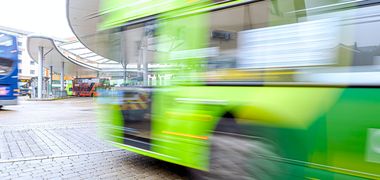 Ein grüner Bus fährt durch einen Busterminal und verschwimmt durch eine Langzeitbelichtung ein bisschen.