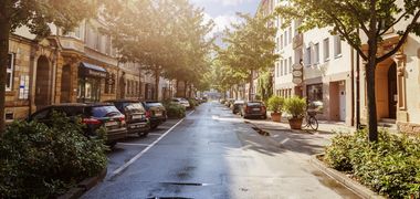 Blick in die sommerliche Alexanderstraße in Bayreuth – grüne Bäume, parkende Autos.