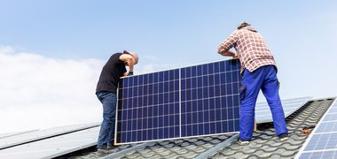 Handwerker installieren ein Solarpanel auf einem Dach.
