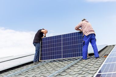 Handwerker installieren ein Solarpanel auf einem Dach.