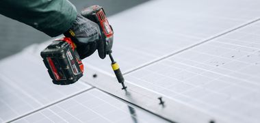 Nahaufnahme wie eine Person mit einem Akkuschrauber Solarpaneele befestigt.