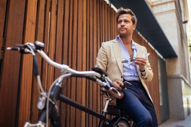 Ein Mann im Jackett lehnt auf seinem Fahrrad und schaut nach vorn.
