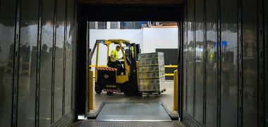 Aus dem Inneren eines Lastwagen heraus ist ein Arbeiter zu sehen, der mit einem Gabelstapler Paletten verlädt.