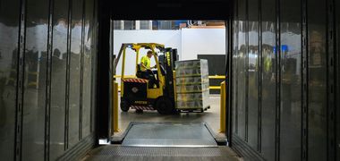 Aus dem Inneren eines Lastwagen heraus ist ein Arbeiter zu sehen, der mit einem Gabelstapler Paletten verlädt.