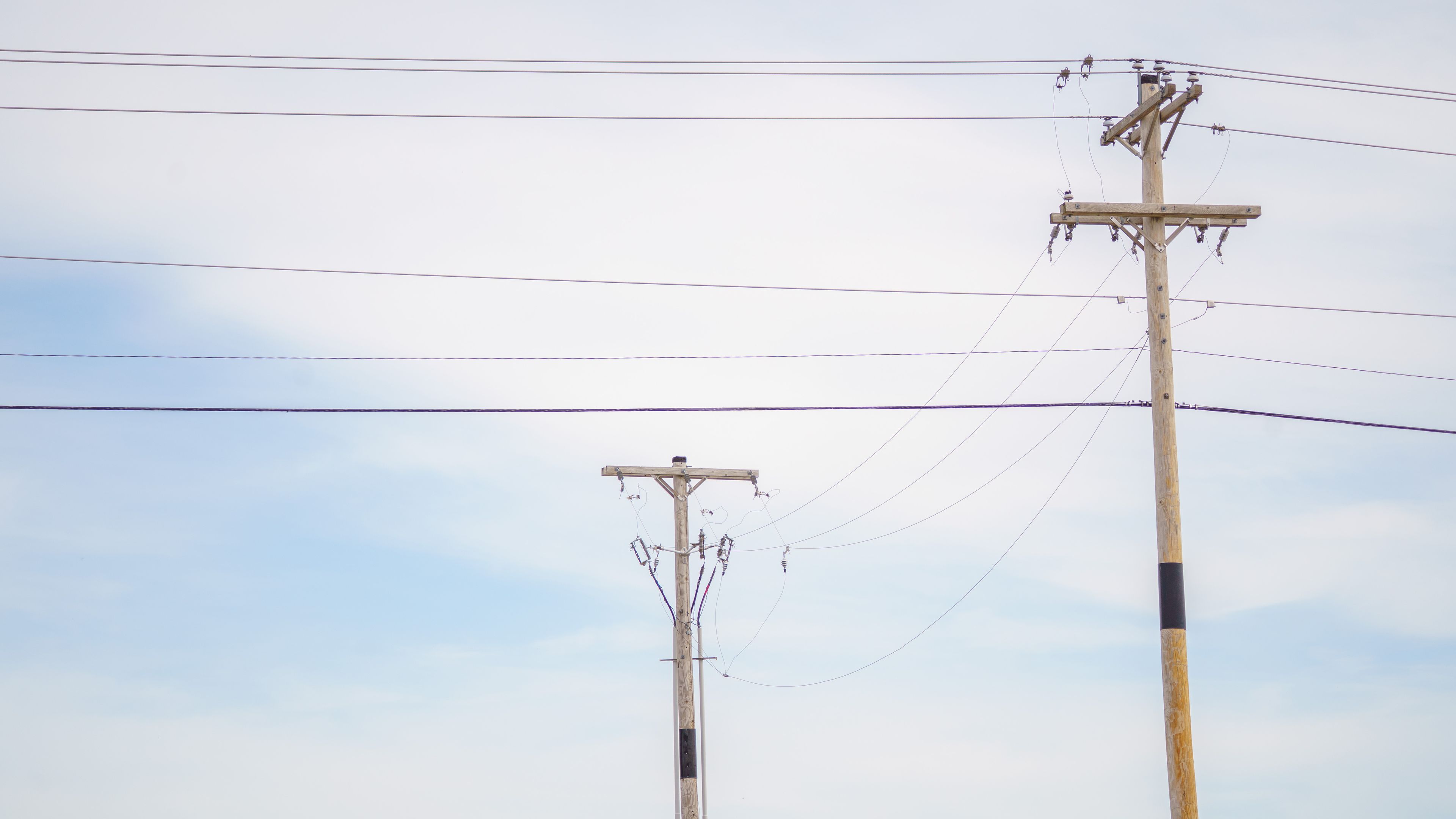 Two wooden utility poles with multiple power lines against a cloudy blue sky.