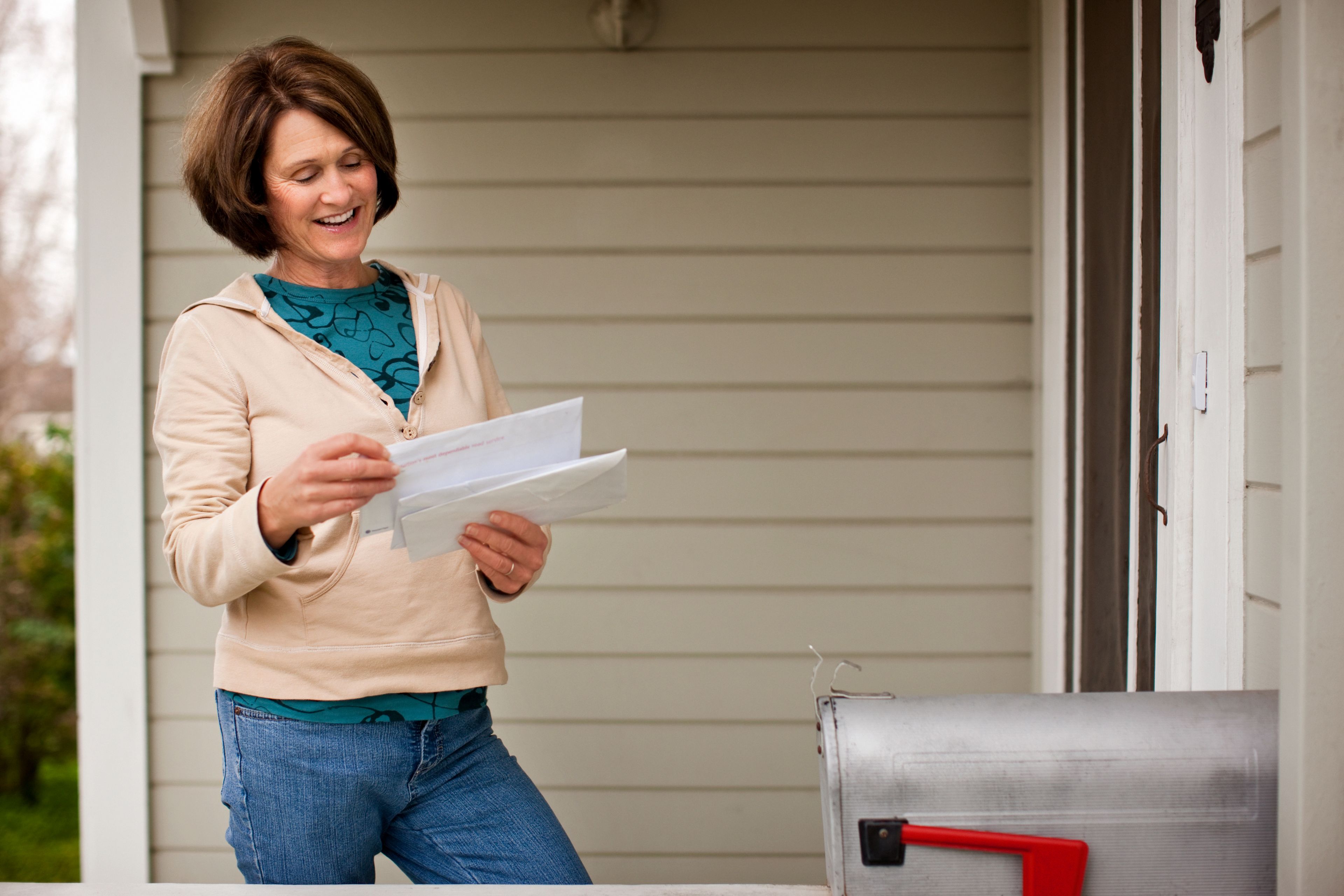 A woman wearing a hoodie, happily checking her mail on her porch