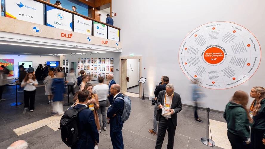 People mingling in a conference lobby with company logos on the wall and a large circular chart.