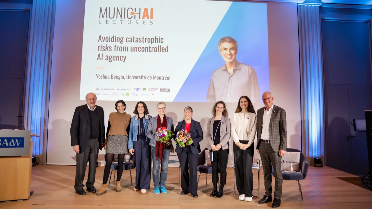 Eine Gruppe von Menschen steht auf einer Bühne vor einer großen Leinwand, auf der „Munich AI Lectures“ und Veranstaltungsdetails angezeigt werden.