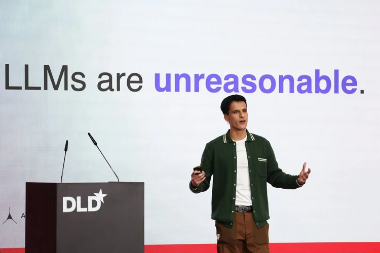 Person speaking on stage with a presentation slide reading "LLMs are unreasonable." DLD logo on the podium.