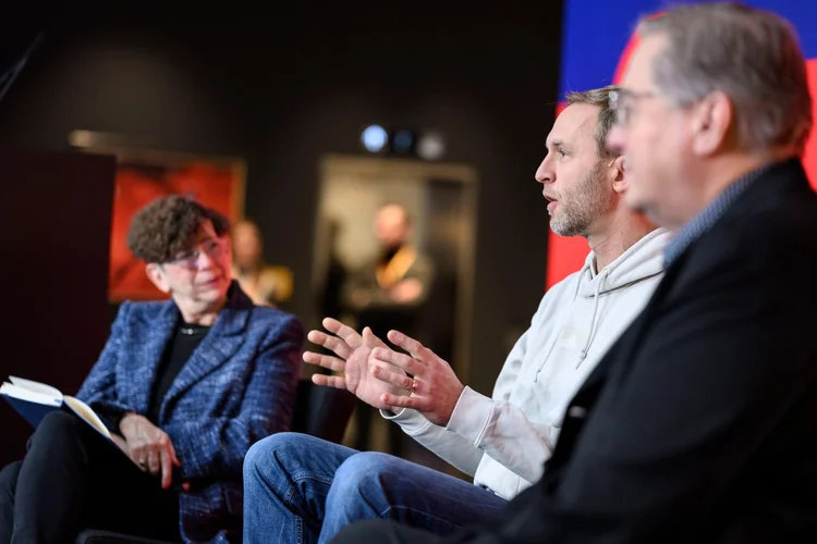 Three people engaged in a panel discussion; one is speaking while the others listen attentively.