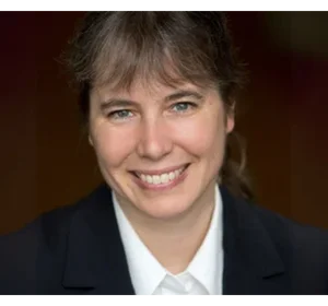 Gitta Kutinyok mit langen braunen Haaren, bekleidet mit einem dunklen Blazer und einer weißen Bluse, vor einem dunklen Hintergrund.