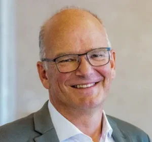 Michael Klimke mit Brille, im Anzug und weißem Hemd, vor neutralem Hintergrund.