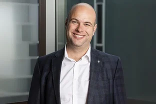 Prof. Sebastian Scherer in Anzug und weißem Hemd steht an einem Fenster, mit unscharfem Hintergrund.