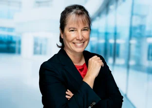 Prof. Dr. Gitta Kutyniok in einem schwarzen Blazer mit verschränkten Armen, stehend in einem hellen, modernen Büro mit Glaswänden.