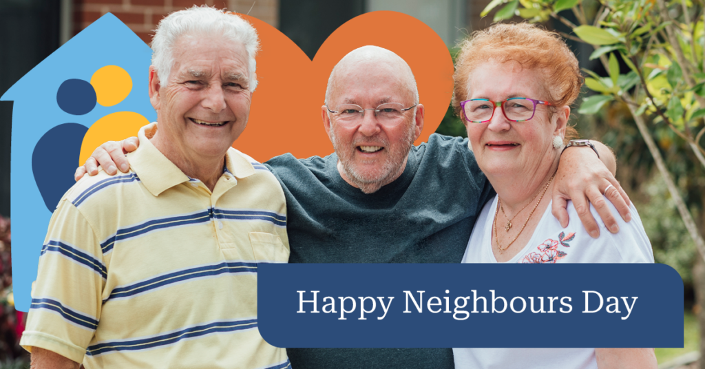 Three smiling older adults stand together with arms around each other. A sign reads "Happy Neighbours Day" in front of them.