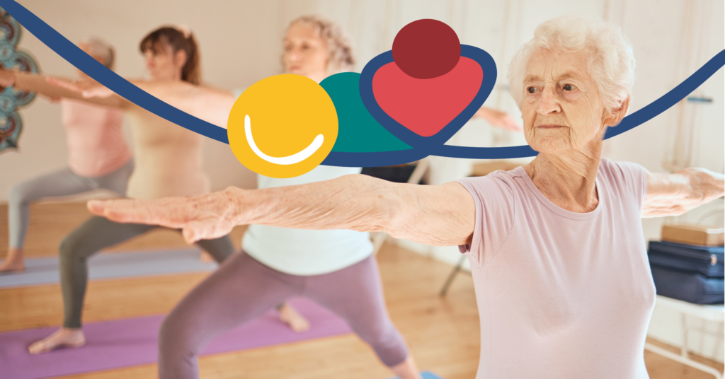 Elderly women practicing yoga in a bright room, with one woman in focus extending her arms in a warrior pose.