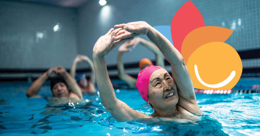 Elderly individuals in a pool exercise class, wearing swim caps and stretching with arms raised, smiling and engaged.