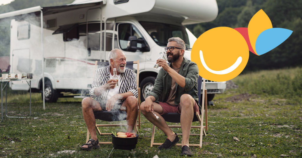 Two men sitting on chairs, enjoying drinks and grilling near a camper van in a grassy area, with a colorful logo overlay.