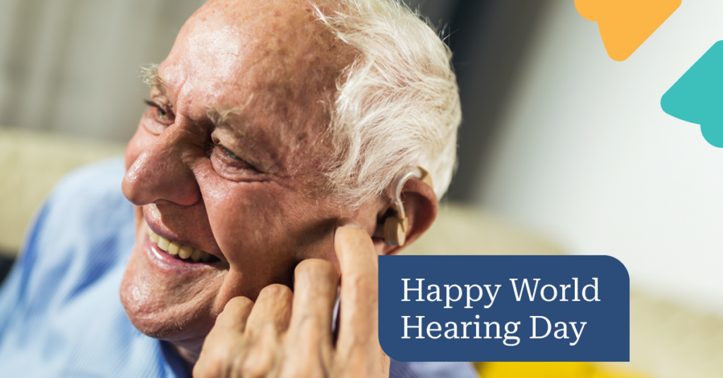 Elderly man smiling while adjusting his hearing aid. Text reads "Happy World Hearing Day" with colorful shapes in the corner.