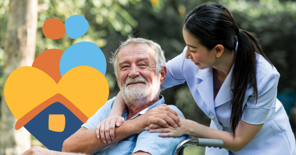 Elderly man in a wheelchair smiles while a caregiver in uniform leans over, outdoors. A heart and house logo is visible.
