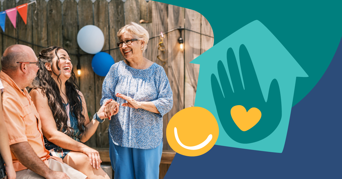 Three people smiling and talking outdoors near a wooden fence with balloons. A graphic of a hand and heart is on the right.