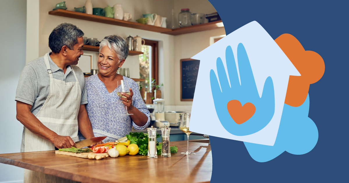 Older couple cooking together, smiling at each other in a kitchen. Ingredients and wine on the counter. Graphic of a heart in a hand on the right.