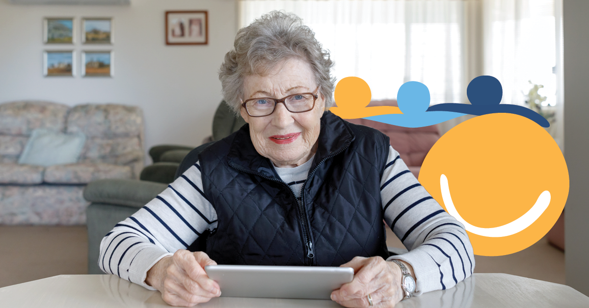 Elderly woman with glasses using a tablet, seated in a cozy living room with a colorful abstract logo in the background.