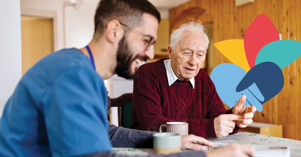 Elderly man in a red sweater and a younger man with glasses sit at a table, smiling, with colorful abstract shapes in the background.