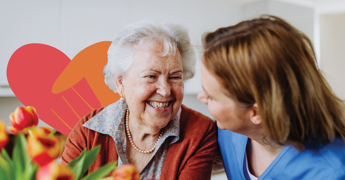 Elderly woman smiling at a caregiver in a blue uniform, with tulips in the foreground and a heart graphic in the background.